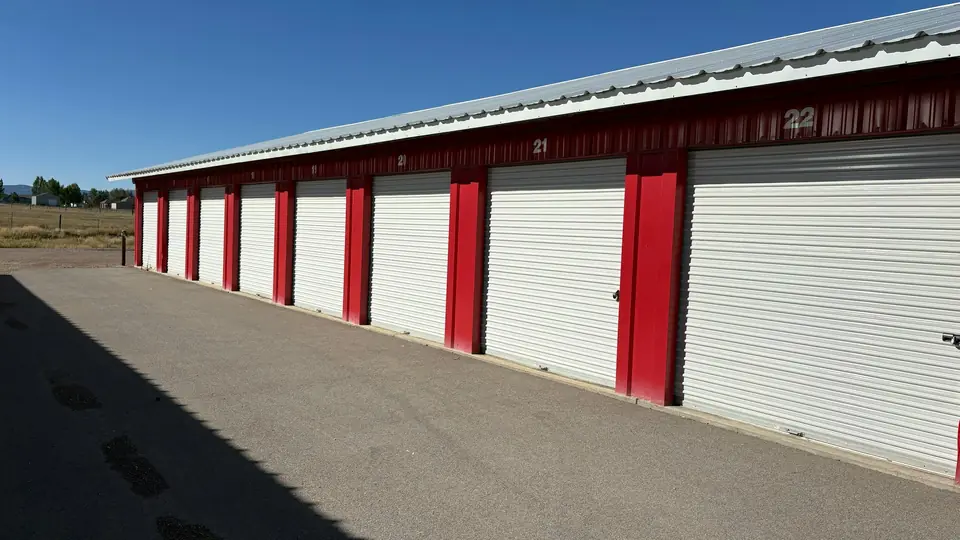 A long row of self-storage units with white roll-up doors and red trim under a blue sky